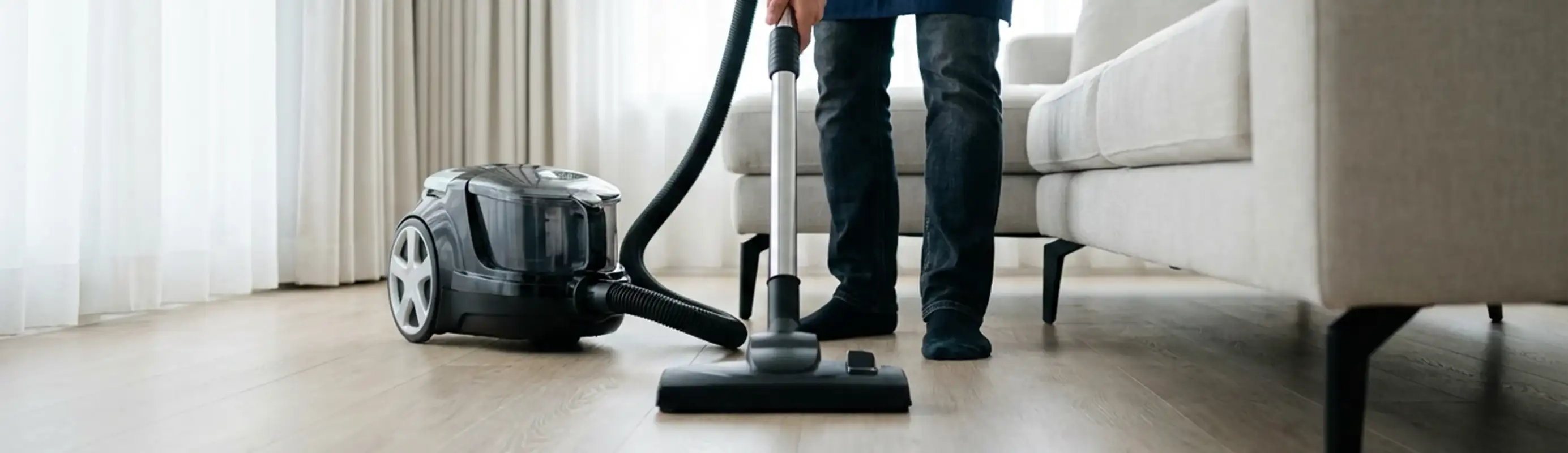 Professional house cleaner vacuuming a living room floor with a canister vacuum cleaner, Lowell, MA.