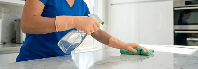 Maid service worker spraying and wiping a kitchen countertop with a microfiber cloth for sanitizing, Lowell, MA.
