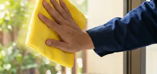 House cleaner wiping a glass window with a yellow microfiber cloth for streak-free cleaning, Lowell, MA.
